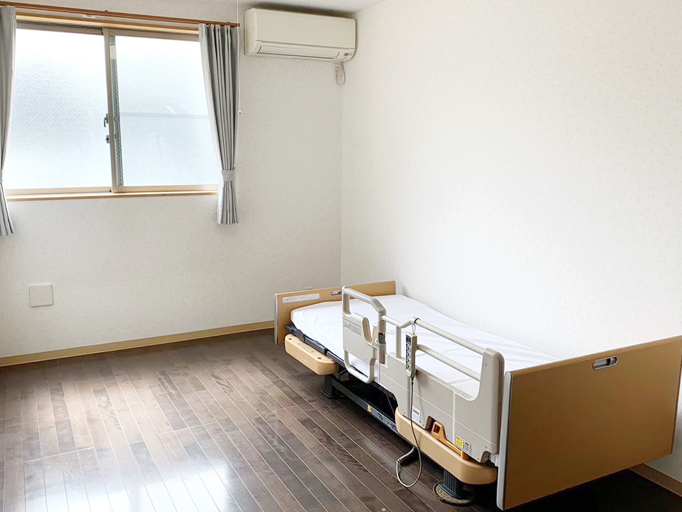 介護用電動ベッドが設置された居室。窓からの採光と冷暖房設備完備。
