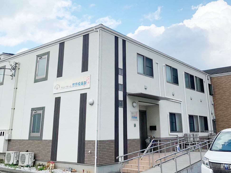 白と褐色のモダン2階建て介護施設。エントランスとスロープが見える